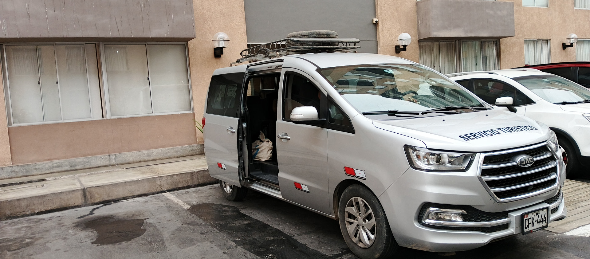 Van JAC M4 plateada con puerta lateral abierta y parrilla de techo cargada